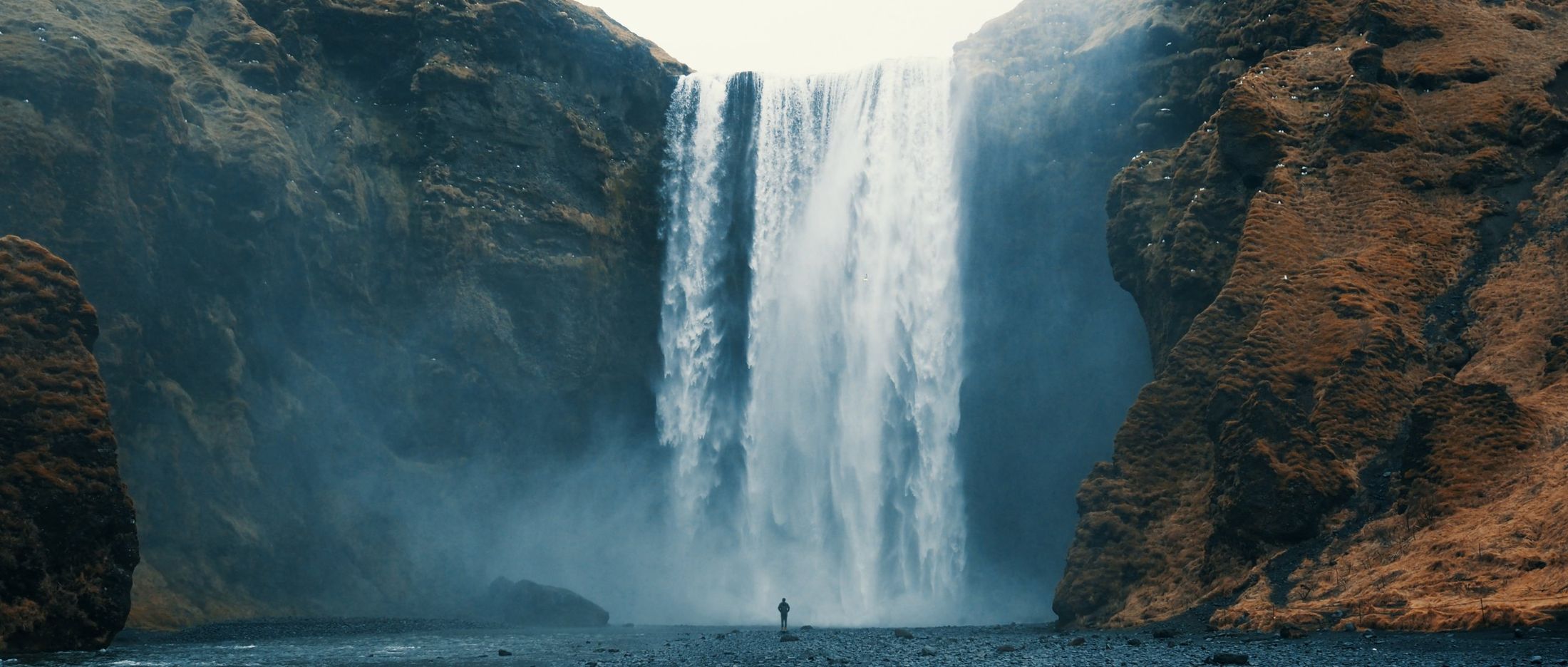 A person dwarfed by a massive waterfall